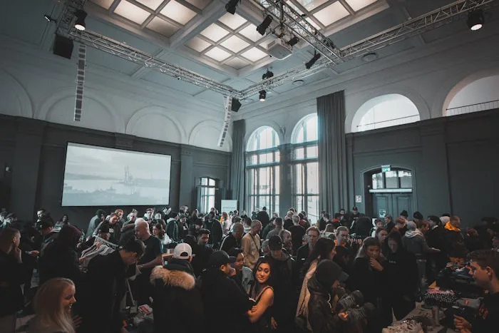 A large crowd enjoys a creative arts conference with a projection screen visible in the spacious event hall.