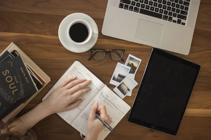 A person journaling with a laptop, book and coffee represents creative writing services at CAQA Creative.