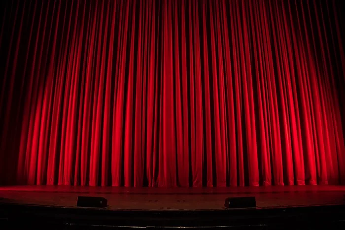 A red stage curtain suggests performing arts services offered by CAQA Creative.