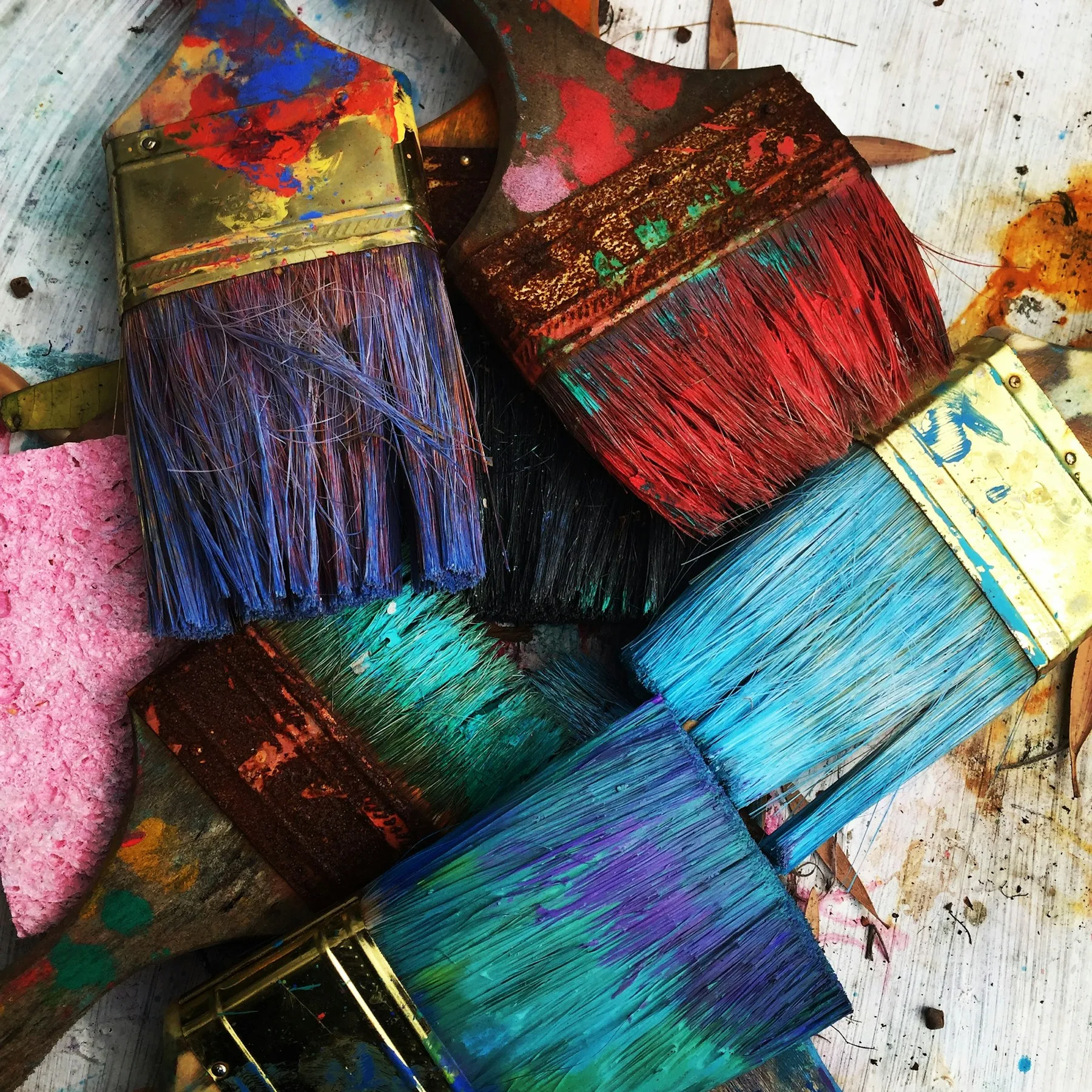Used paintbrushes and a pink sponge rest on a colorful, splattered surface showcasing visual arts.
